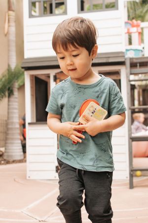 Young child in green shirt walking on outdoor pavement.