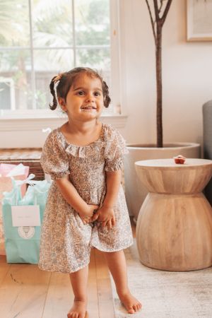 Child in sparkly dress explores party decorations in modern living room with wooden furniture.