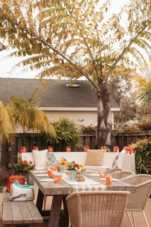Outdoor party setting with wicker chairs and gingham tablecloths under autumn trees.