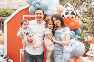 Family poses together in front of red barn backdrop with blue and orange balloon garland.