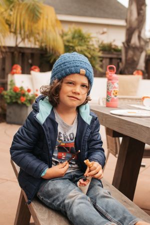 Child in denim jacket and blue beanie sitting at outdoor party table.