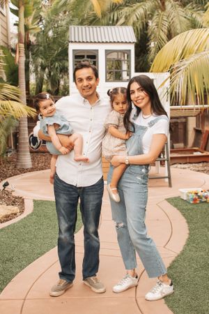 Family photo on garden path with playhouse and palm trees in background.