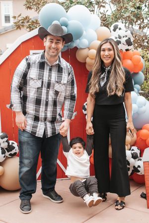 Family poses together at festive party with balloon arch and farm-themed decorations.