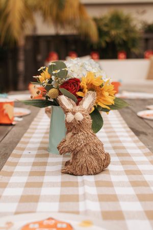 Rustic fall centerpieces with straw decorations and flowers on a checkered tablecloth.