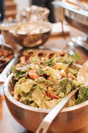 Fresh green salad with vegetables served in wooden bowl at party buffet table.