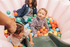 Children play in a pink inflatable ball pit filled with colorful plastic spheres.