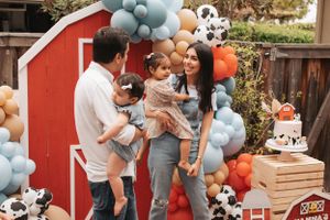 Family celebrating in front of red barn backdrop with festive balloons and party decorations.