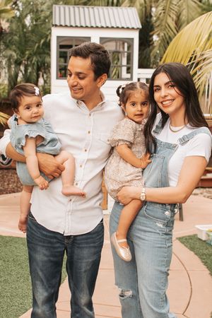 Casual family portrait in tropical garden setting with white playhouse structure.
