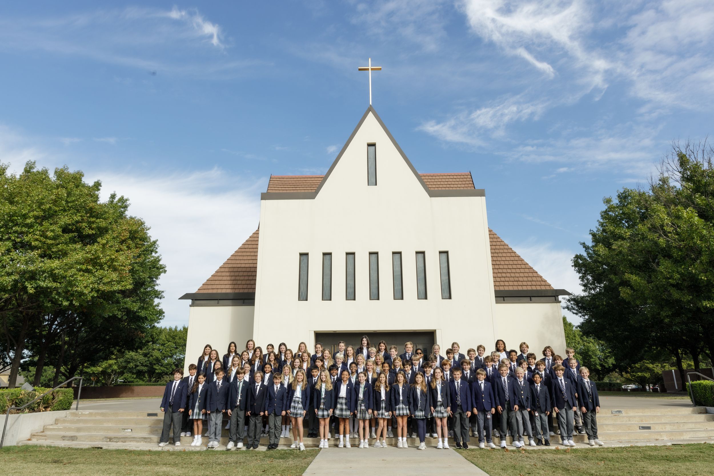 Wide shot of a modern white church building with a large group gathered outside.