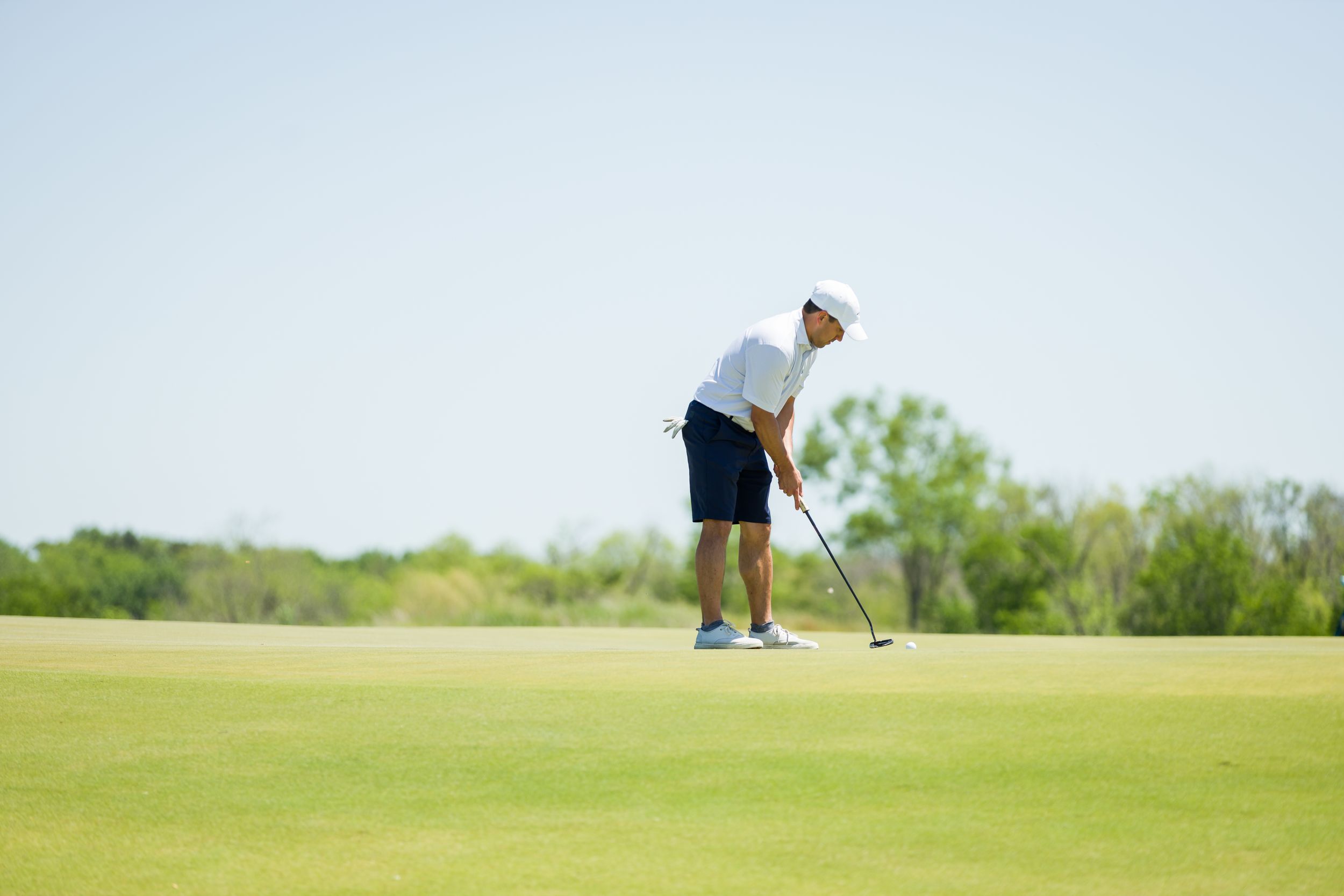 Golfers putting on a manicured green course under bright blue skies.