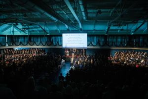 Dark auditorium filled with seated attendees during a large indoor event.