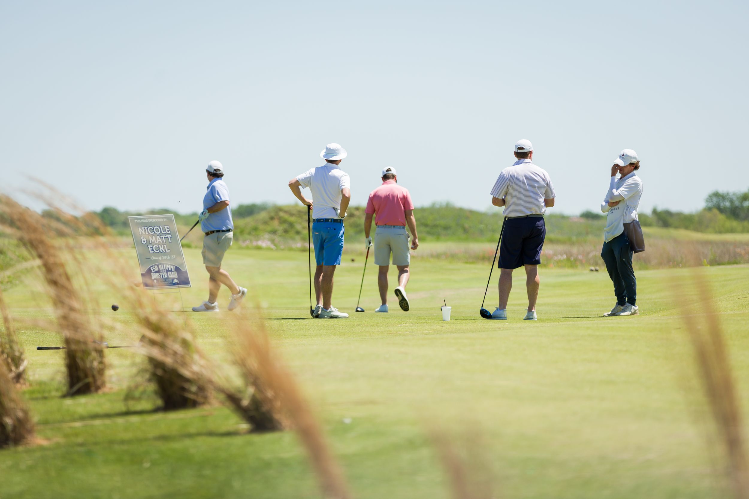 Golfers scattered across a scenic golf course during daytime play.
