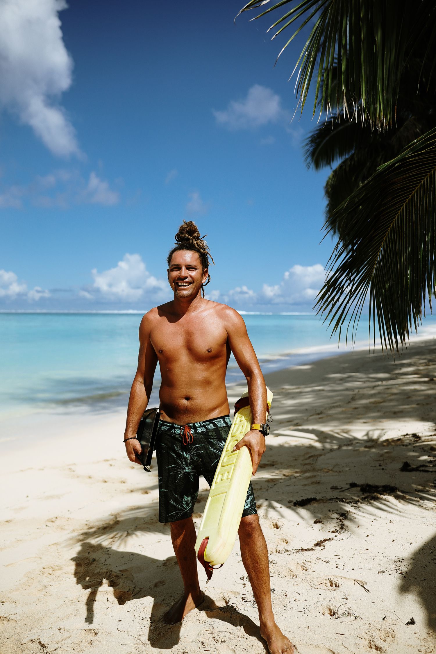 Surfer with surfboard enjoying a sunny day on a tropical beach with palm trees and turquoise waters.