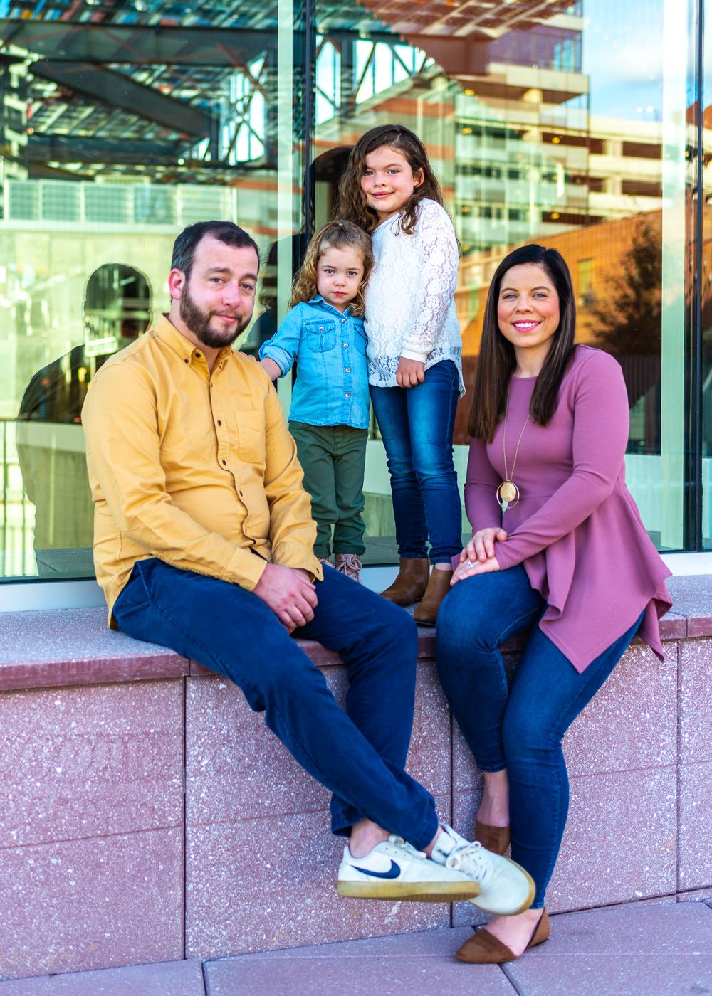 Family of four posing casually against modern glass building exterior.