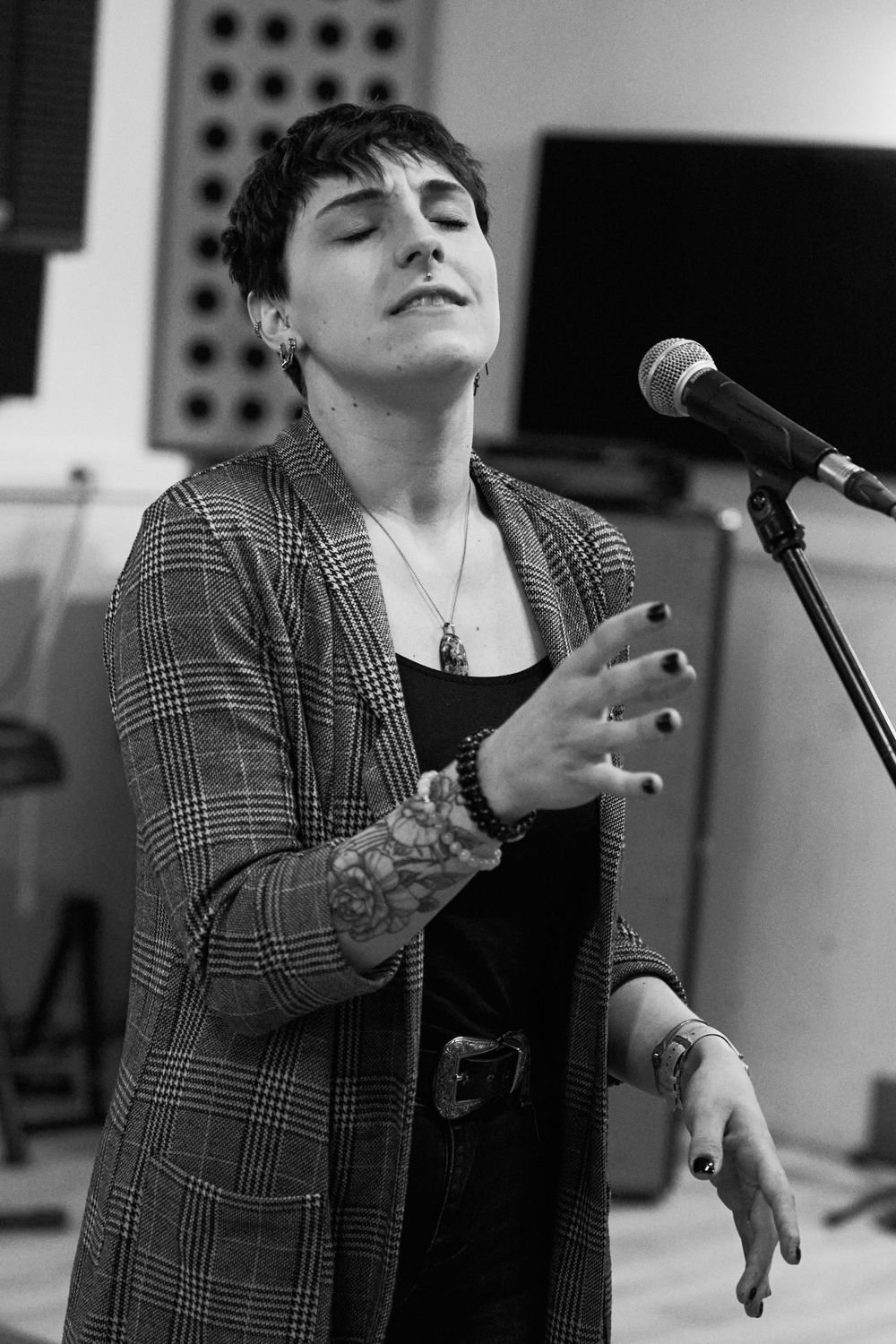 Black and white portrait of performer singing with microphone in plaid blazer.