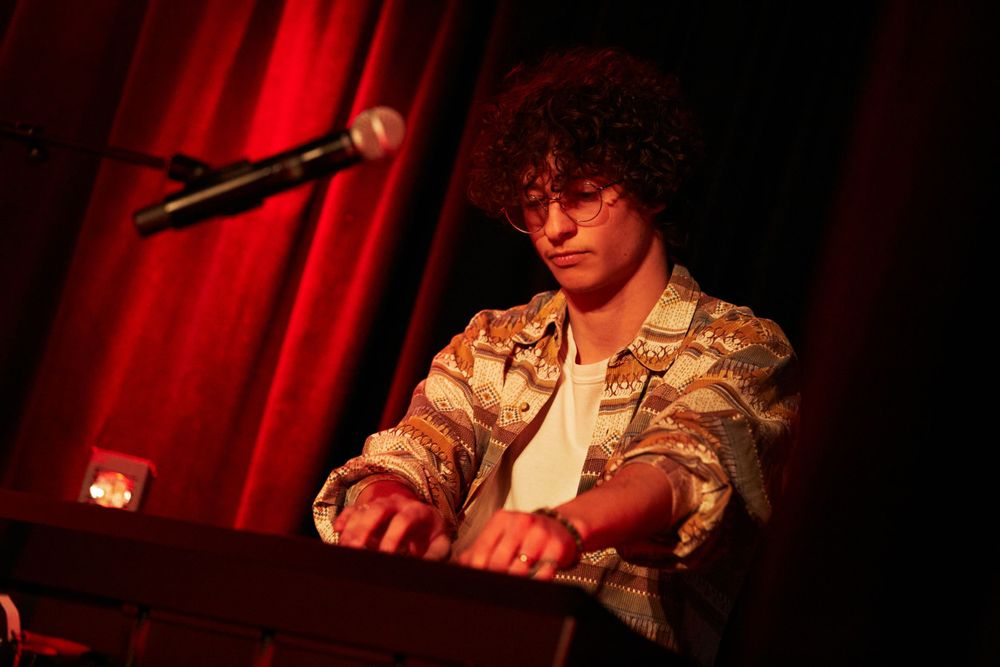 Musician playing keyboard under dramatic red stage lighting.
