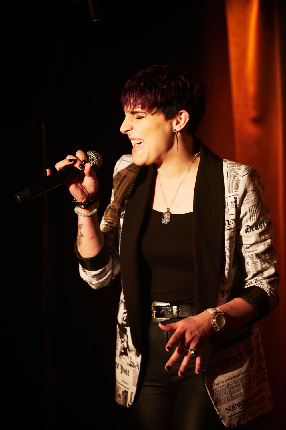 Performer singing passionately on stage wearing a patterned blazer over black outfit.