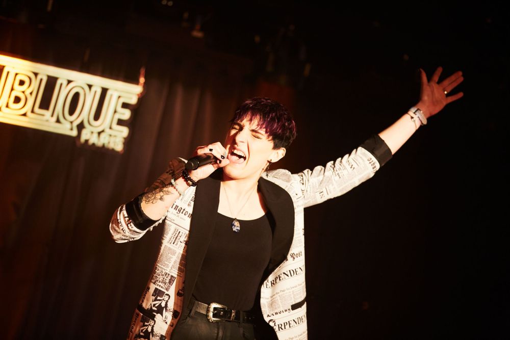 Energetic stage performance with dramatic lighting and performer in sparkly jacket.