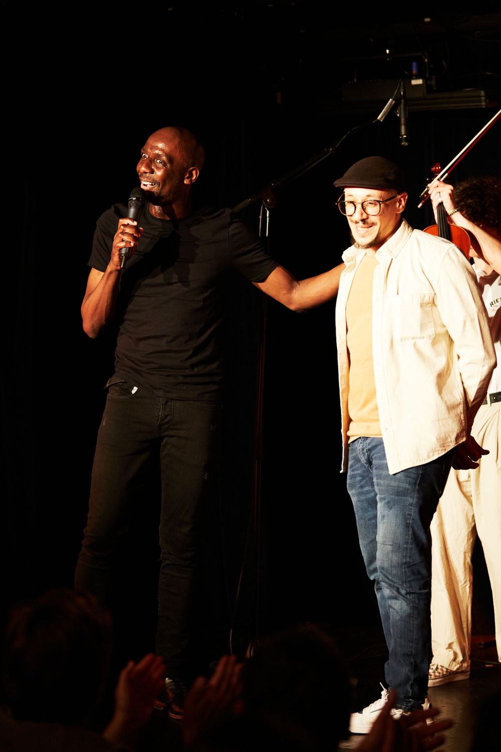 Two performers energetically entertaining crowd on dark stage with microphone.