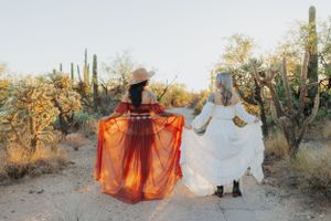 Rust and white dresses flow dramatically against a desert backdrop with saguaro cacti.