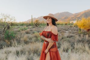A rust-colored dress flows elegantly against desert mountains and autumn foliage.