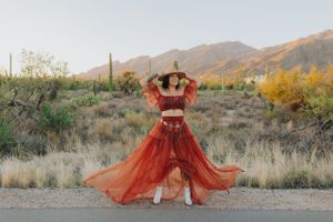 A flowing rust-colored dress creates movement against desert mountains at golden hour.