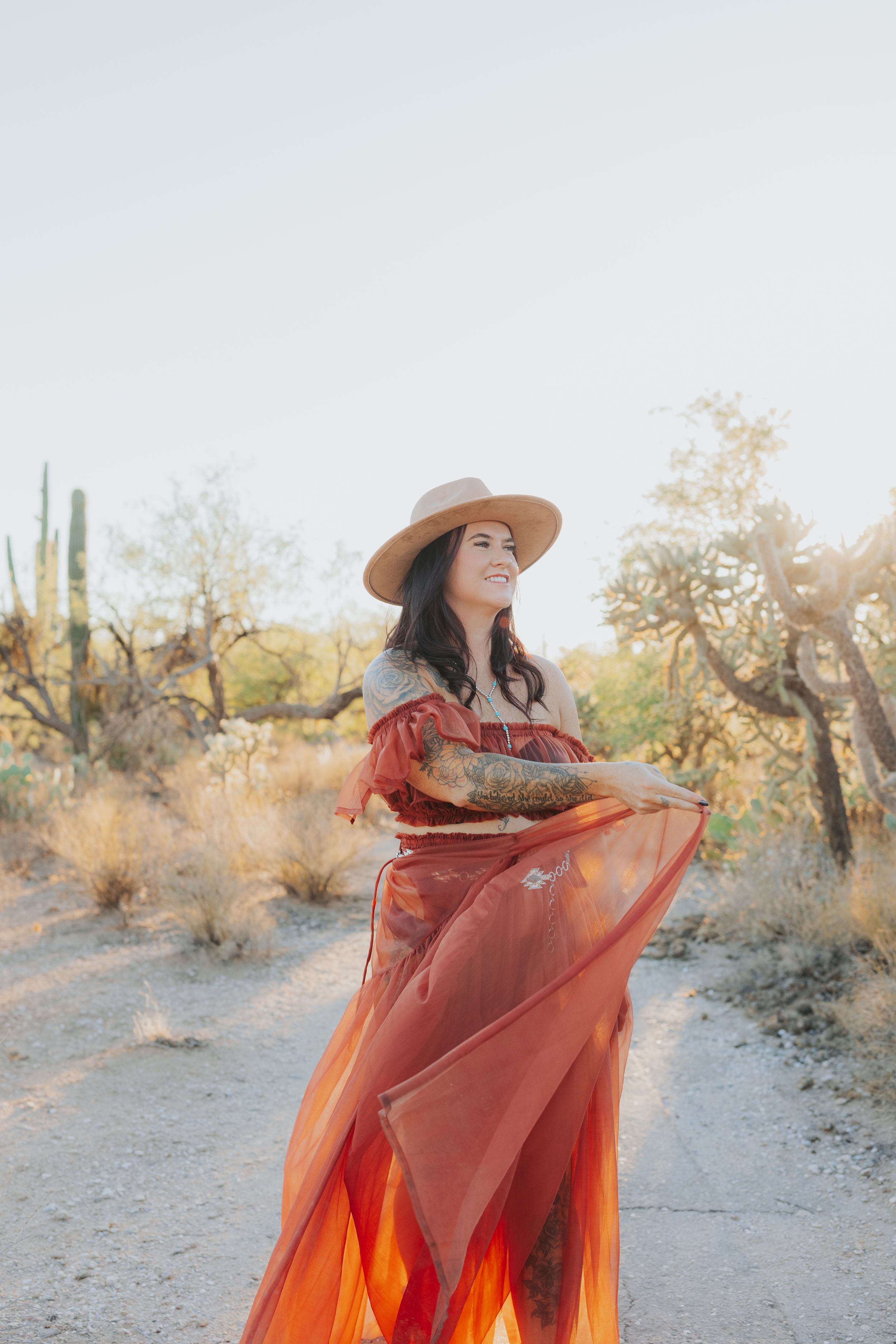 Ethereal desert photoshoot with flowing orange dress and saguaro cacti.