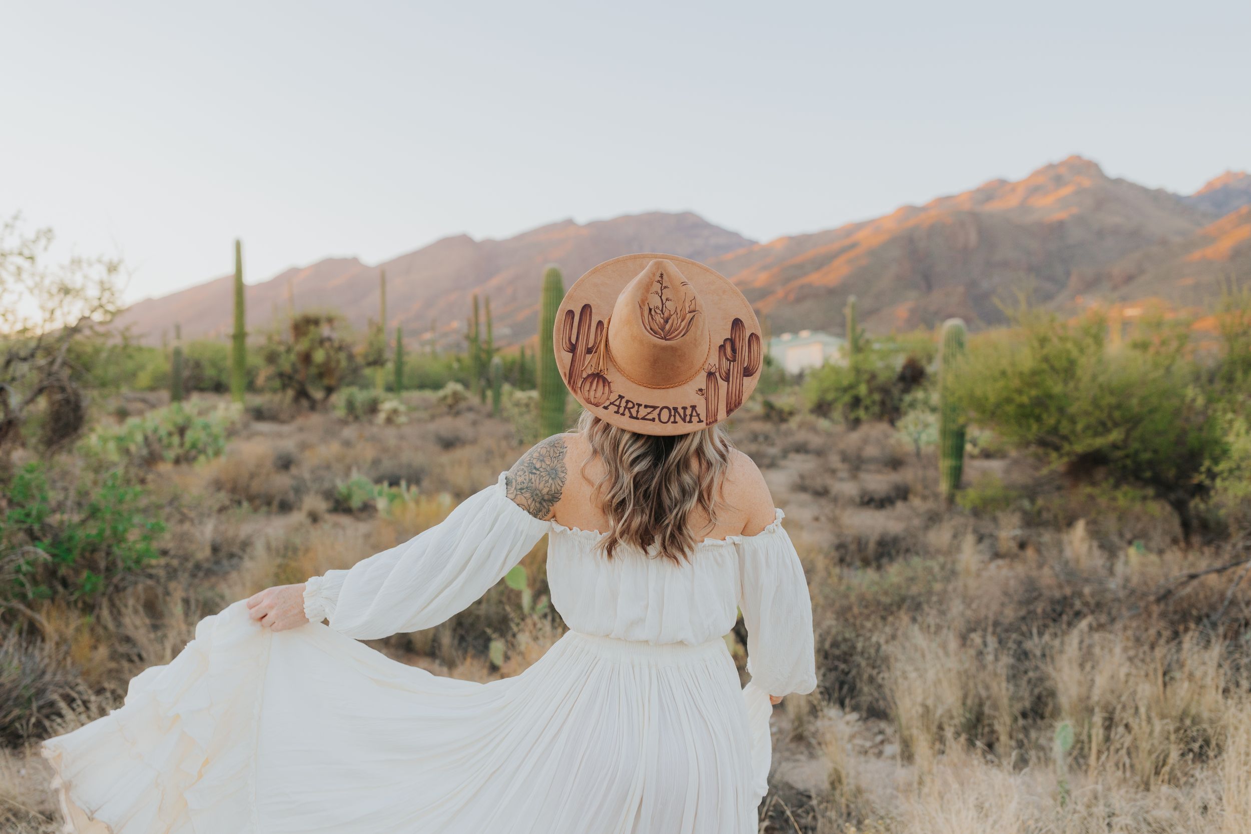 Flowing white dress photographed against desert mountains and cacti at sunset.
