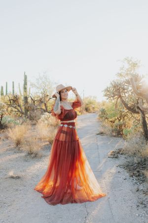A flowing red and orange dress catches golden light on a desert path lined with saguaro cacti and desert flora.