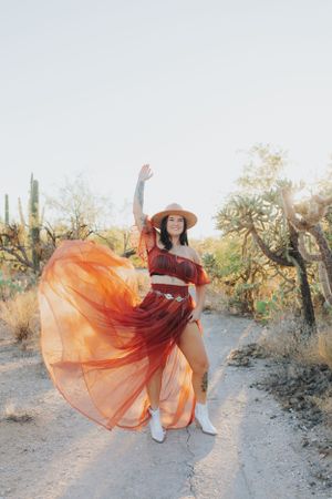 A flowing red dress twirls dramatically against a desert landscape with cacti and setting sun.