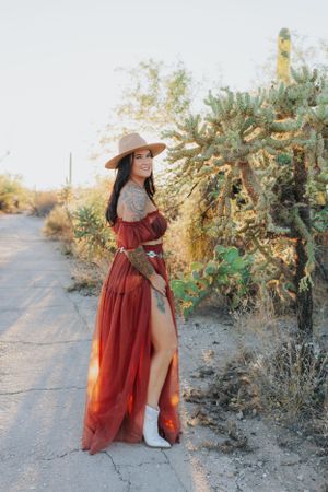 A red flowing dress contrasts with white boots on a desert trail surrounded by cacti.