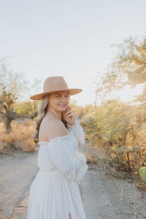 An ethereal white dress and tan hat create a romantic desert photoshoot aesthetic.