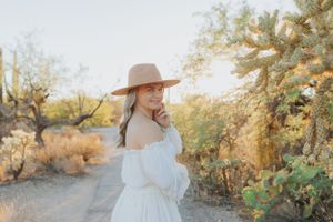 A dreamy off-shoulder white dress glows in golden desert light among cacti.