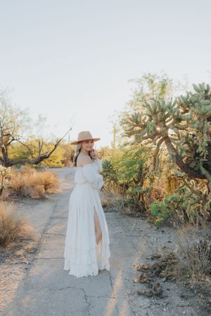 A flowing white dress catches light on a winding desert path with cacti and desert flora.