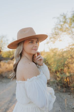 A tan hat and white off-shoulder dress create an elegant desert portrait.