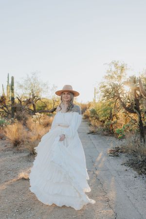 A flowing white dress and tan hat create movement against a desert landscape.