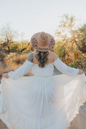 A white ruffled dress flows in the breeze against a desert backdrop with cacti and warm sunset light.