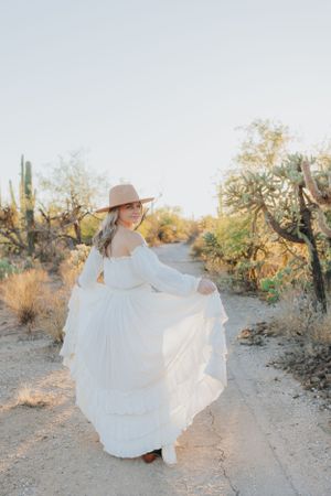 A flowing white maxi dress spins dramatically in a desert setting with saguaro cacti and natural lighting.
