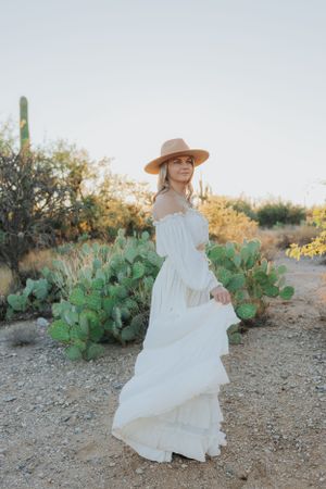 A flowing white dress creates movement against desert terrain with cacti and natural desert flora.
