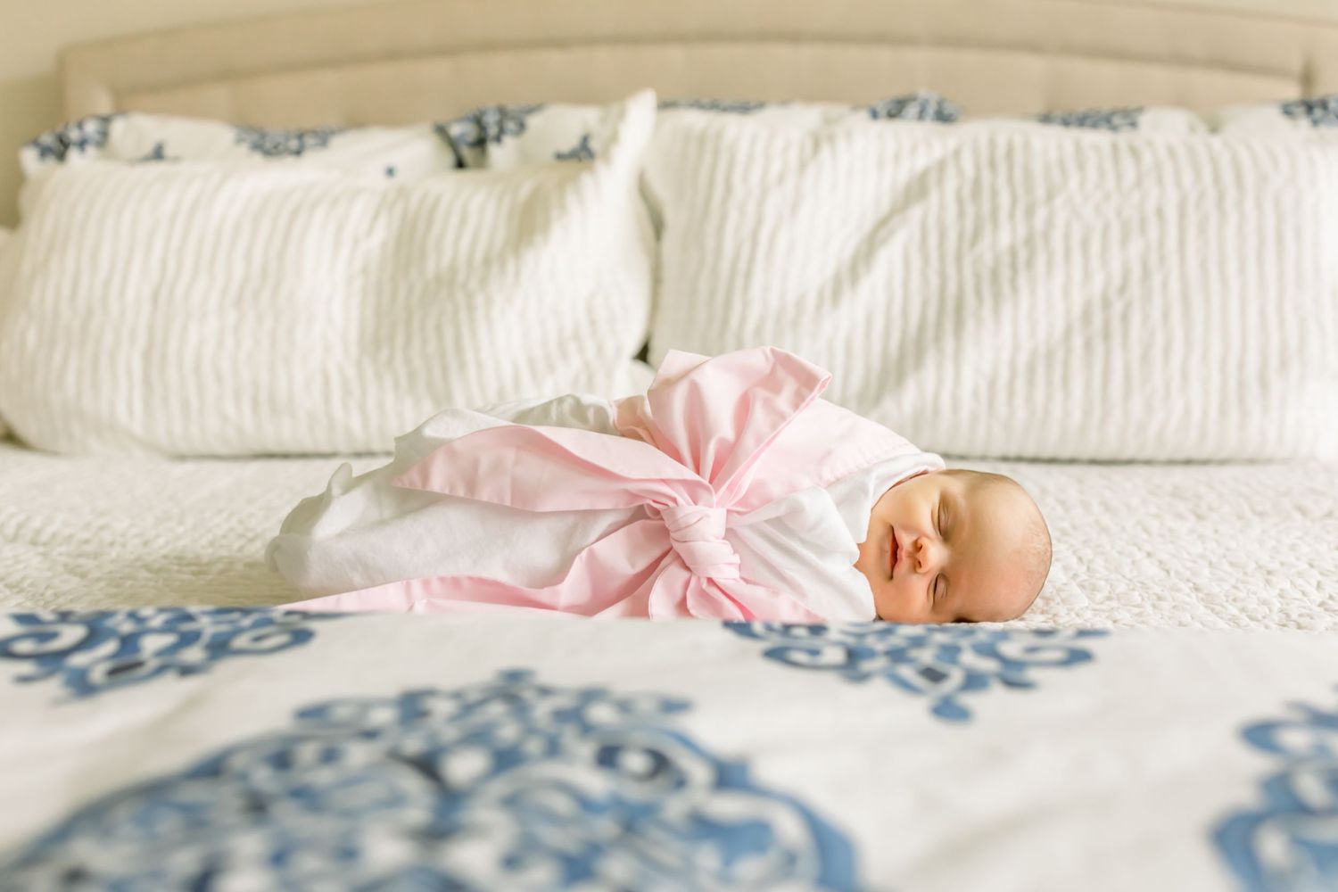 A baby in pink sleepwear lies on a white and blue patterned bed.