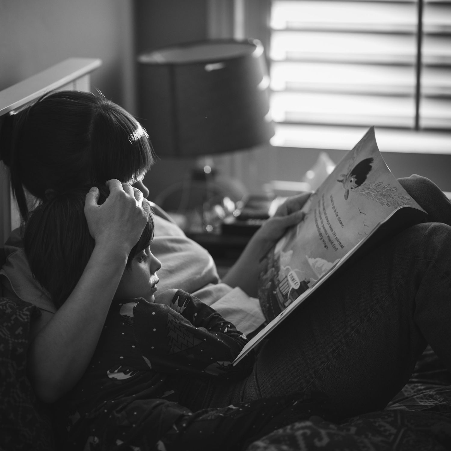 A black and white photo shows someone reading while lying down with a book in a relaxed indoor setting.