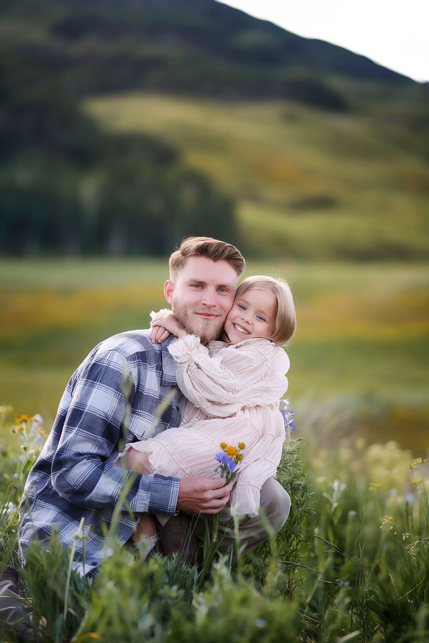 A father hugs his daughter and hands her flowers.