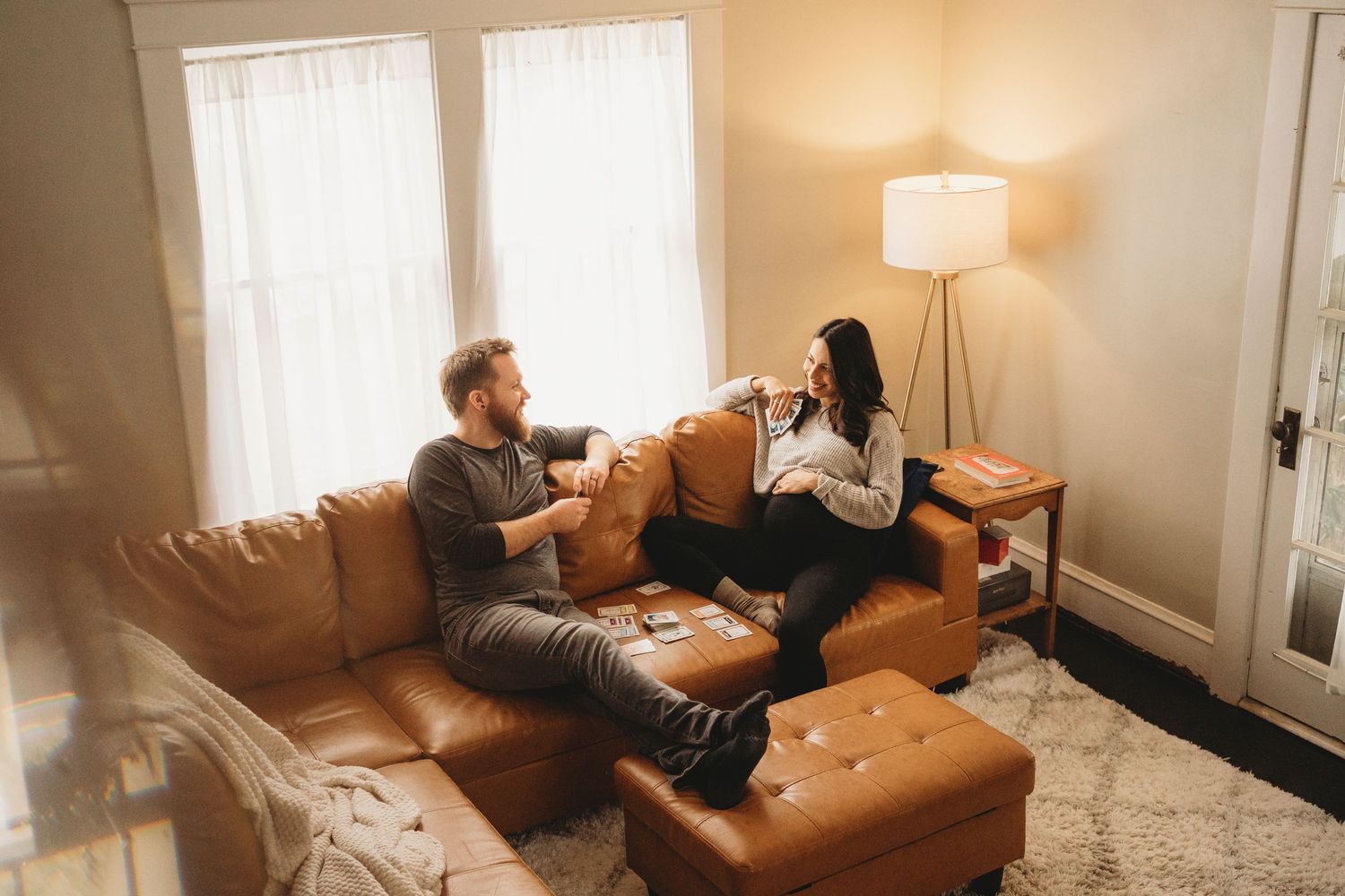 A couple shares quality time together on a tan leather couch in a bright living room.