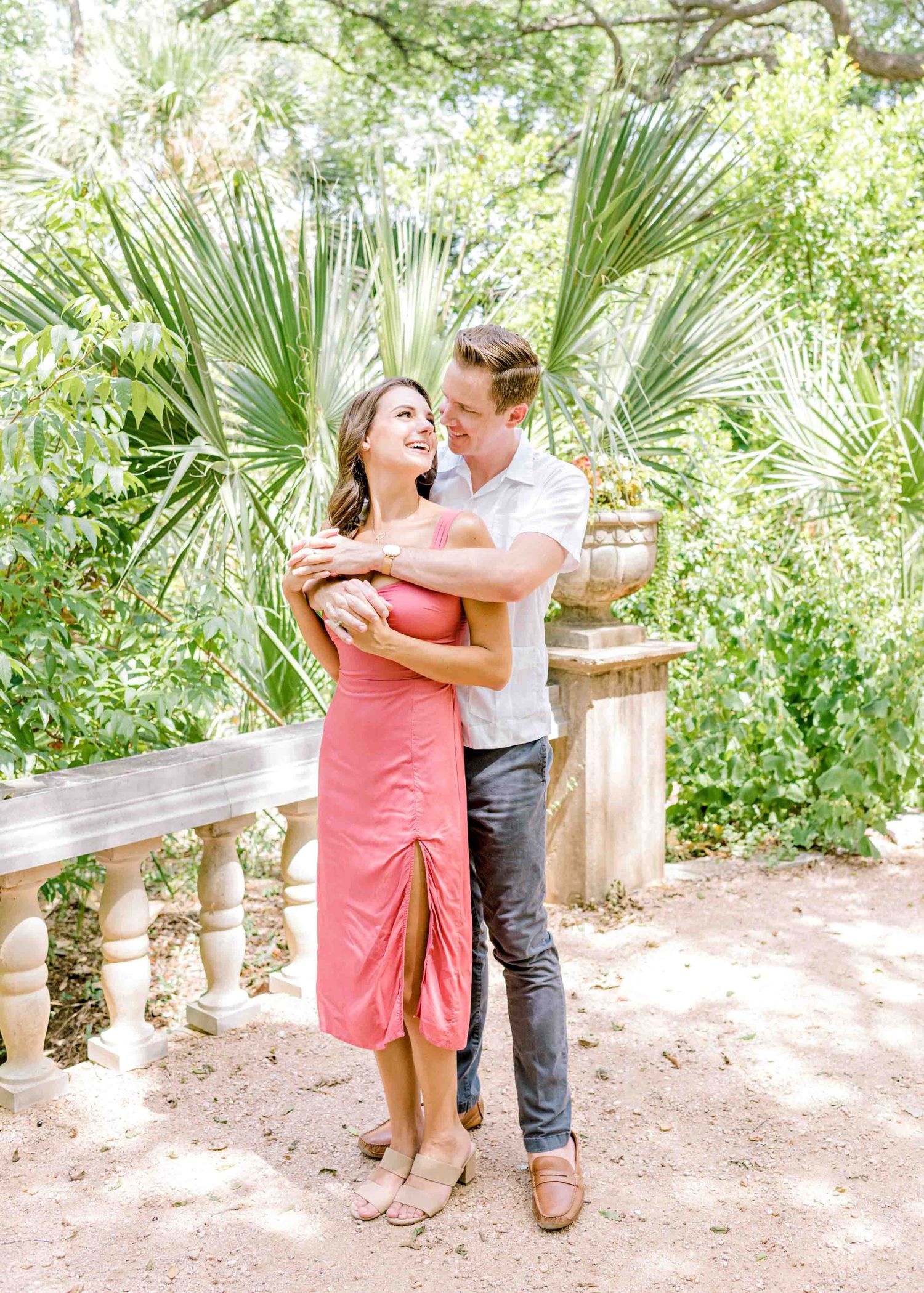A couple shares a joyful embrace among tropical palm plants and garden scenery.