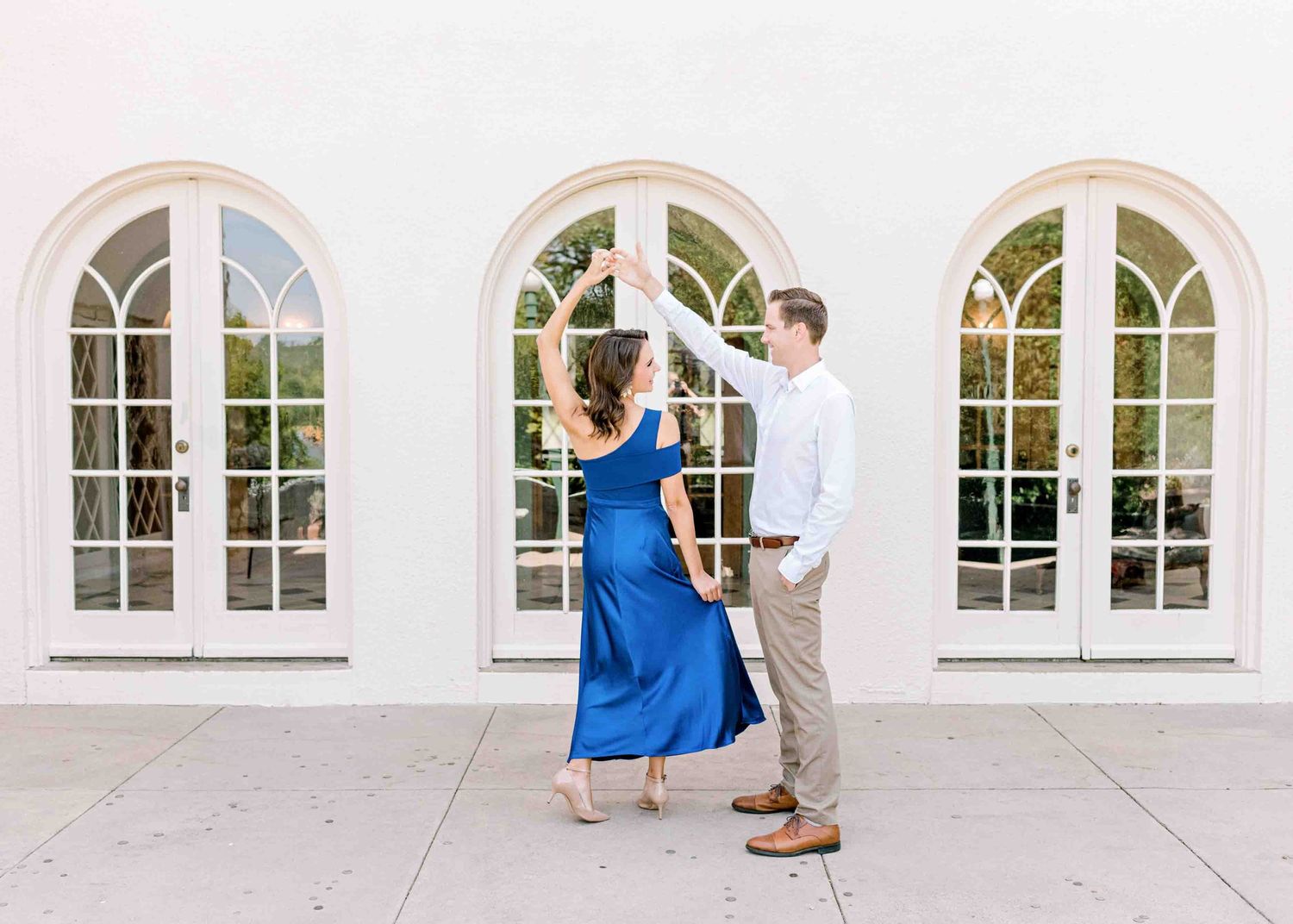A romantic dance pose in front of white arched windows with diamond panes.