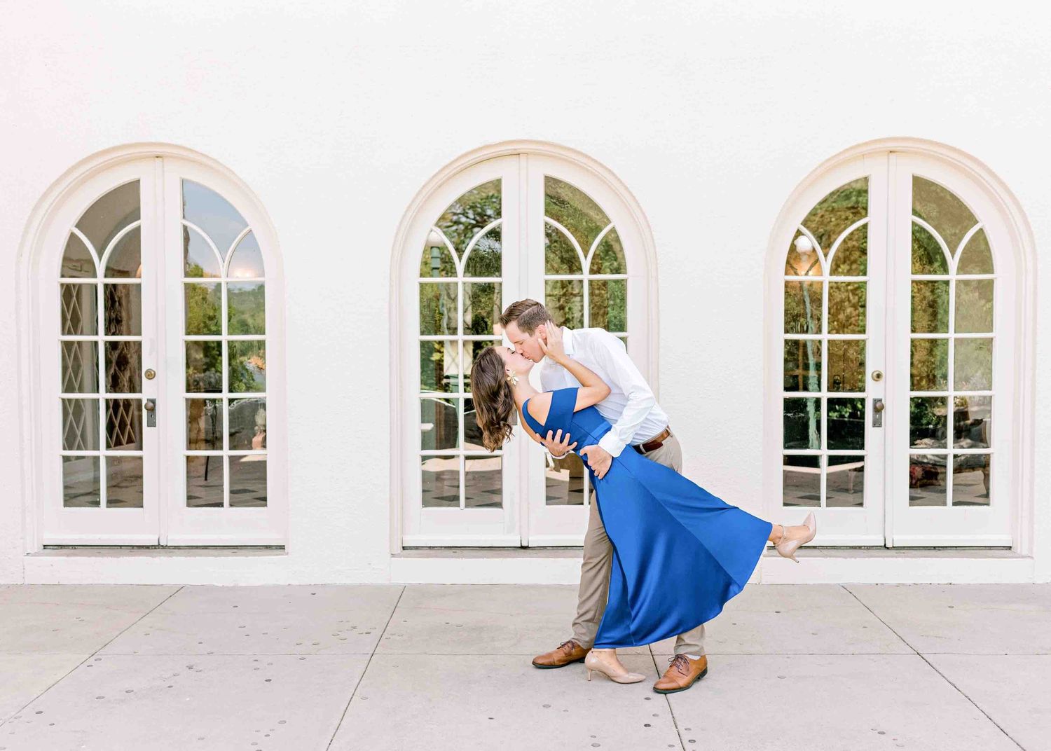 A playful dip pose in front of architectural arched windows.