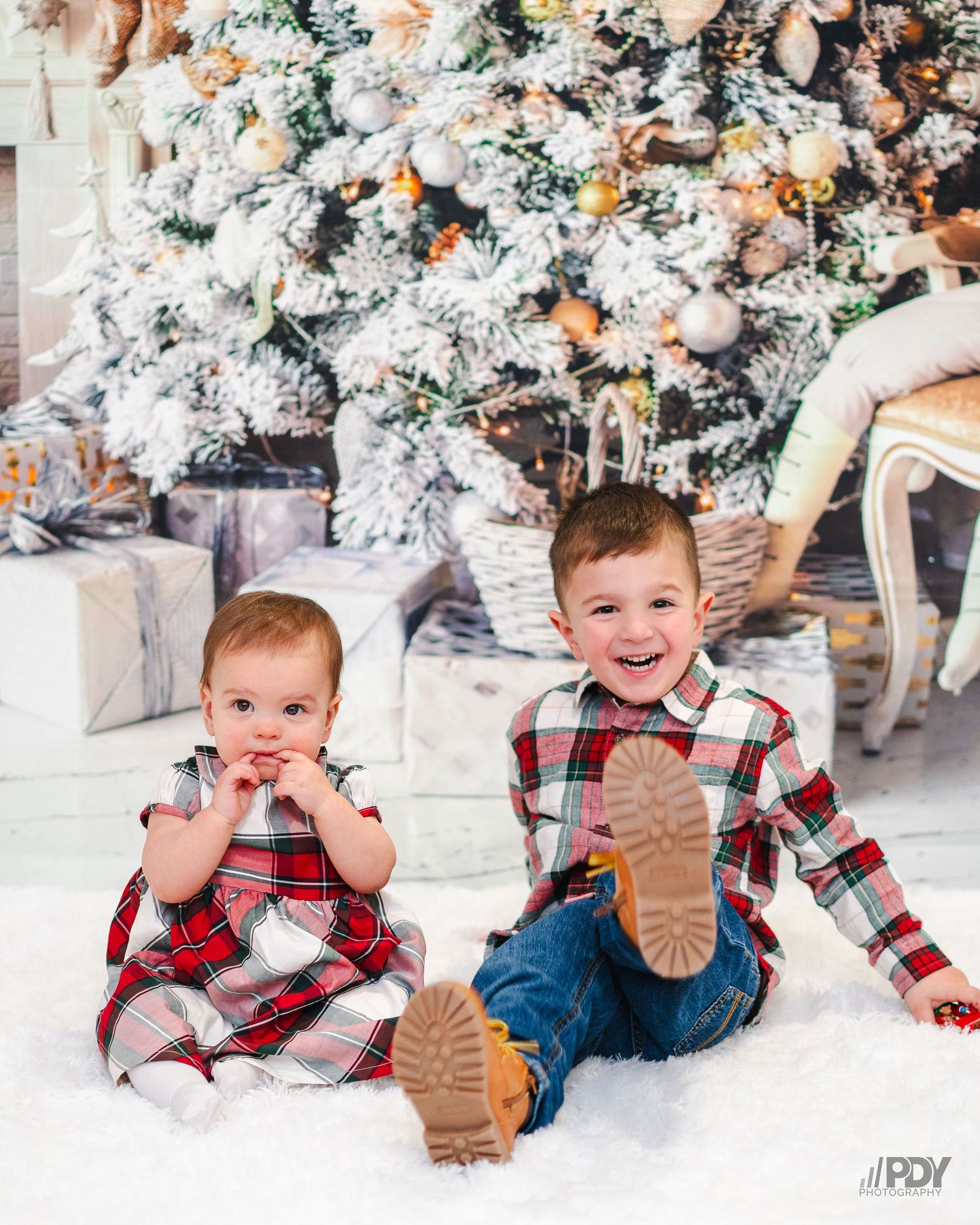 Playful Christmas portraits of a child in plaid crawling and posing by presents and a decorated tree.