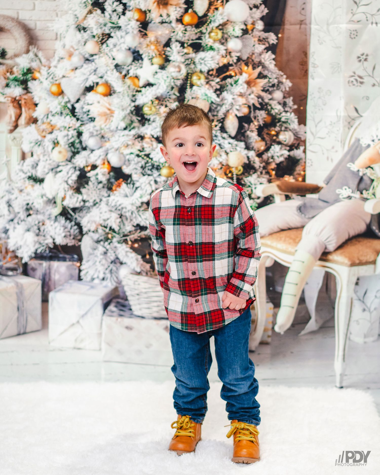 Holiday photos of a toddler in plaid and jeans playing in front of a decorated Christmas tree.