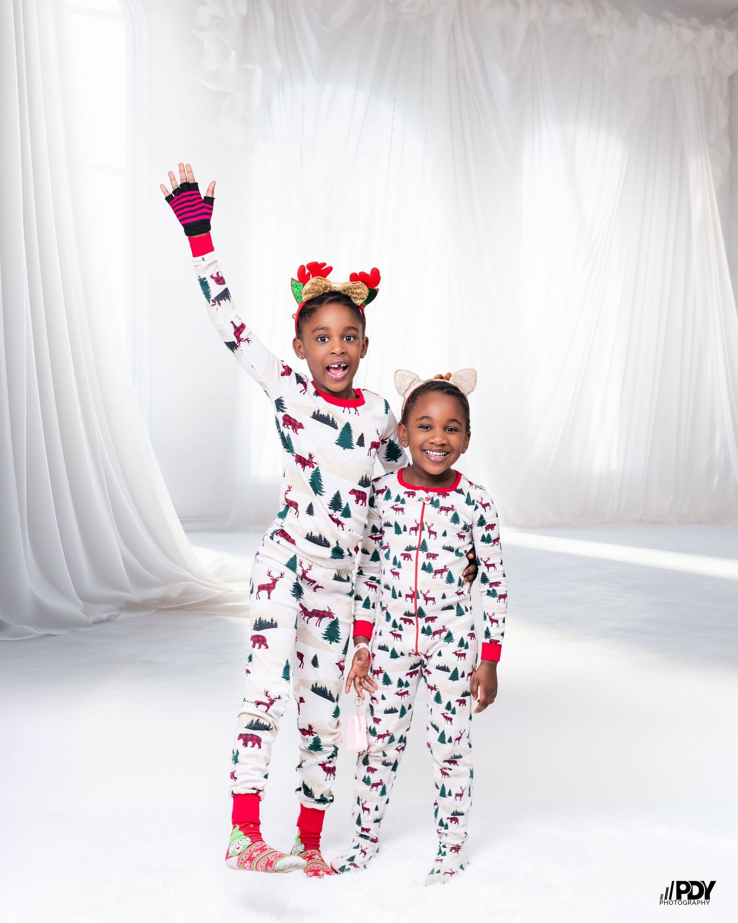 Playful holiday photo of children in matching winter-themed pajamas and reindeer headbands.