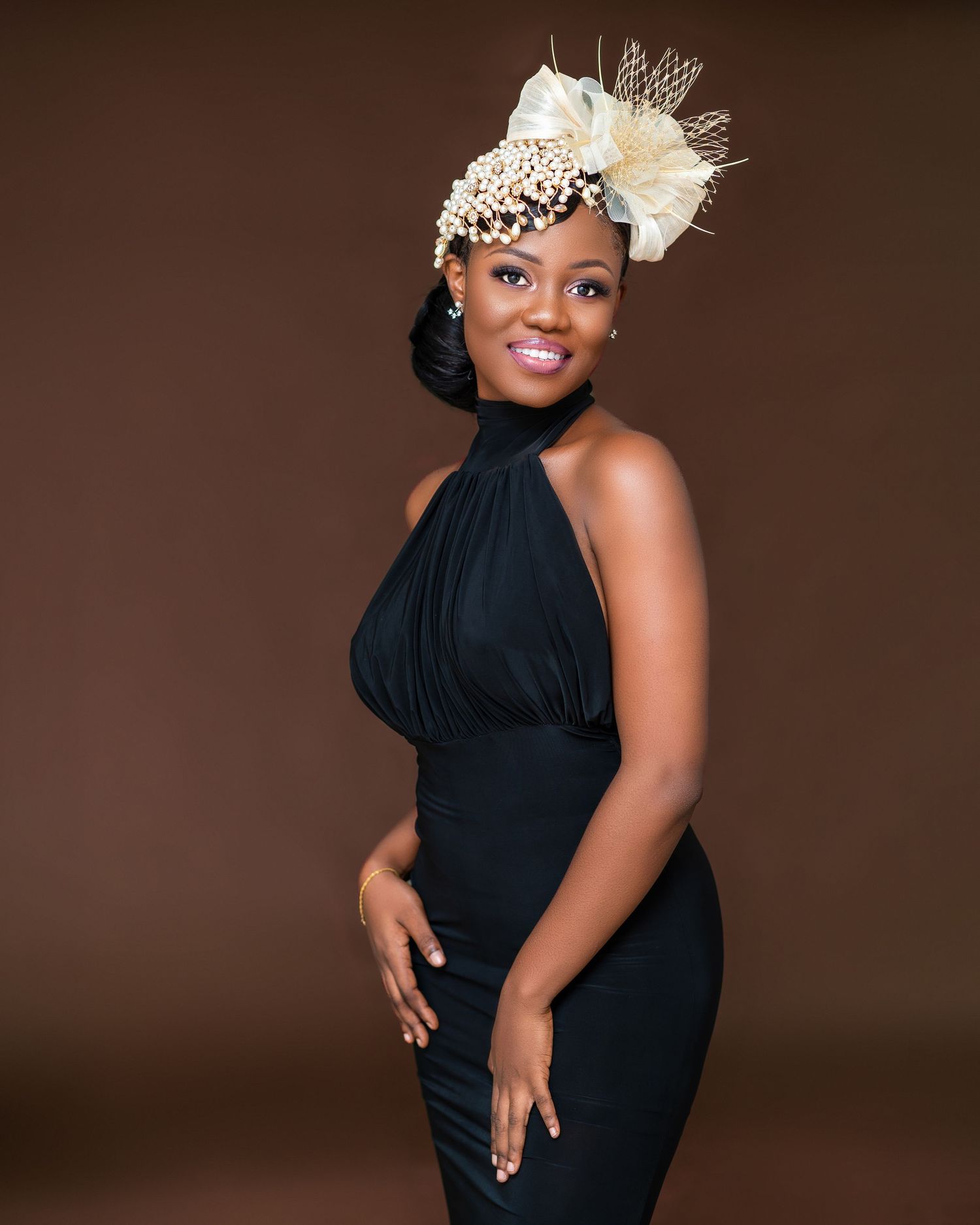 Woman in black dress with elegant feather headpiece poses against dark background.